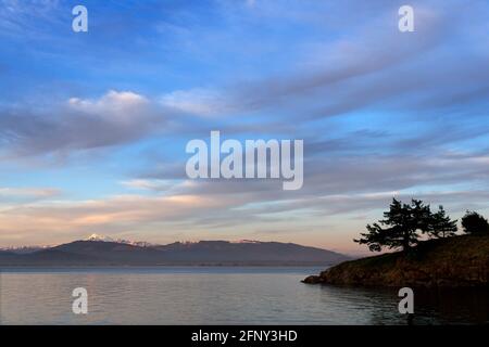 Blick auf eine Landzunge auf Saddlebag Island mit Mount Baker und Cascade Mountains über die Padilla Bay im Hintergrund bei Sonnenuntergang, Saddlebag Island Marine Stockfoto