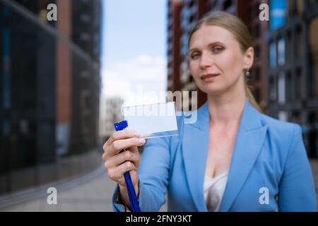 Business stilvolle Frau in einer blauen Jacke hält ein Abzeichen In der Hand vor dem Hintergrund eines Bürogebäudes Stockfoto