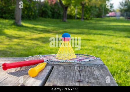 Badminton-Schläger und Federball auf Holztisch mit grünem Gras im Park an einem sonnigen Sommertag. Aktives Lifestyle-Konzept. Spaß machen Stockfoto