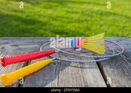 Badminton-Schläger und Federball auf Holztisch mit grünem Gras im Park an einem sonnigen Sommertag. Aktives Lifestyle-Konzept. Spaß machen Stockfoto