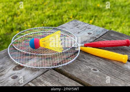 Badminton-Schläger und Federball auf Holztisch mit grünem Gras im Park an einem sonnigen Sommertag. Aktives Lifestyle-Konzept. Spaß machen Stockfoto