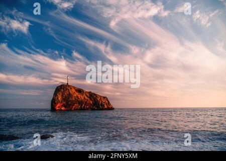 Heller Sonnenuntergang am Meer. Die Wellen stürzen in den Felsen, erleuchtet von dem warmen Sonnenuntergang, Sand und Kieselsteinen, vulkanischem Basalt wie in Island. Meereswelle bricht in Stockfoto