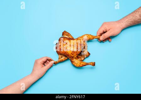 Mann und Frau greifen ein gebratenes Huhn, isoliert auf blauem Hintergrund. Menschen teilen Essen, Konzept. Essen gebackenes Huhn. Kampf um Nahrung. Stockfoto