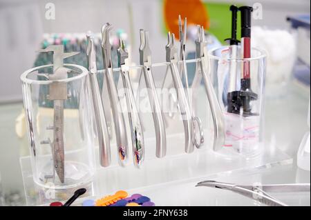 Nahaufnahme von Dentalwerkzeugen, die auf einem transparenten Stativ hängen. Kieferorthopädische Zangen und Zangen auf dem Tisch. Stahlinstrumente für den zahnärztlichen Gebrauch. Konzept der Zahnmedizin, medizinische Instrumente Stockfoto