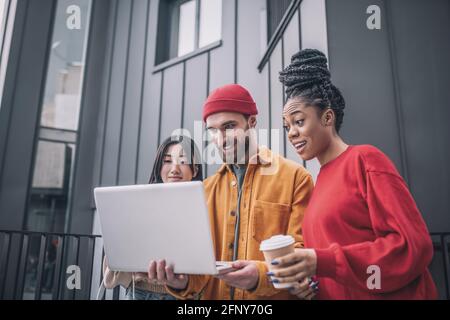 Drei Freunde sehen sich etwas auf einem Laptop an und freuen sich Stockfoto