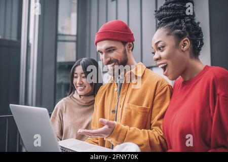 Drei Freunde sehen sich etwas auf einem Laptop an und freuen sich Stockfoto