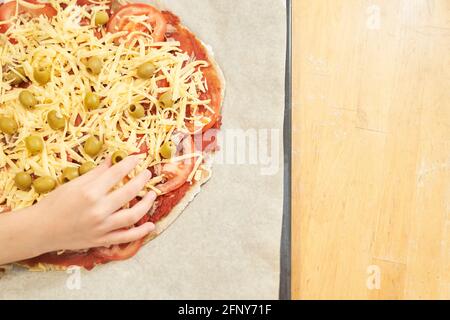 Childs Hand mit Pizza auf Backpapier zum Backen vorbereitet. Gesunde glutenfreie Pizza. Glutenfreier Kochkurs. Foto mit Kopierbereich. Stockfoto