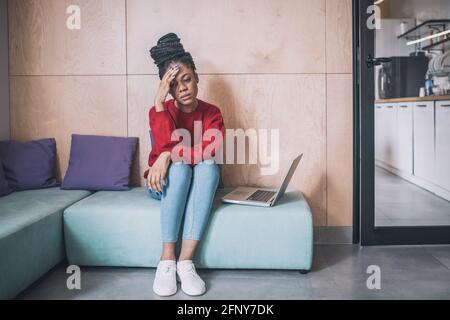 Junge afroamerikanische Frau sitzt und sieht müde aus Stockfoto