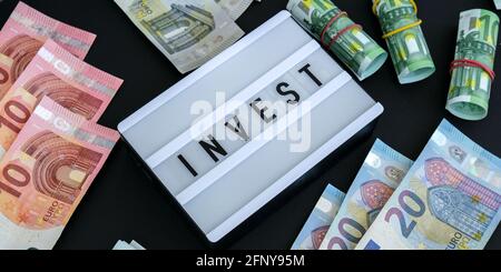 Leuchtkasten mit Wort INVESTIEREN in schwarze Buchstaben um Euro-Banknoten. Geld, Unternehmen, Finanzen, Investitionen, Sparen. Barrechnung. Geschäftsbudget von uns Stockfoto