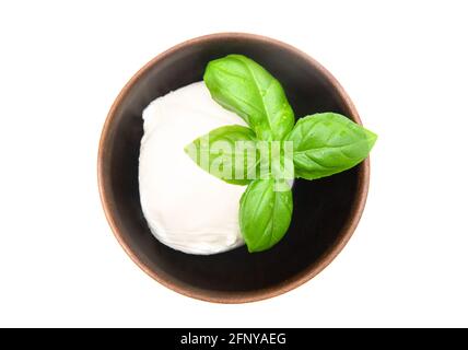 Mozzarella-Kugel mit frischen Basilikumblättern auf der Oberseite in einer kleinen Holzschale isoliert auf weiß. Draufsicht, Nahaufnahme. Stockfoto