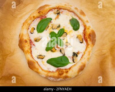 Hausgemachte Meeresfrüchte-Pizza mit frischen Basilikumblättern auf einem Pergament Papier Stockfoto