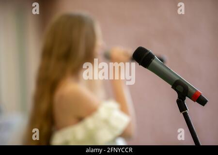 Bühnenmikrofon auf dem Hintergrund des verschwommenen Sängers. Performance oder Rezital. Stockfoto