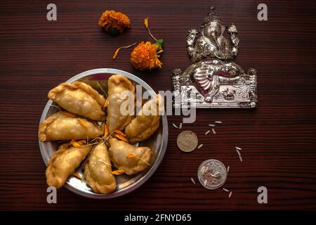 Draufsicht auf ein Idol von Lord Ganesha, das auf einem hölzernen Hintergrund mit süßen Gujiya, Blumen und Münzen für das Diwali-Fest platziert wurde Stockfoto