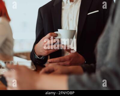 Makrofoto eines Geschäftsmannes in einem Café in einem Anzug, der eine Tasse Kaffee hält. Stockfoto