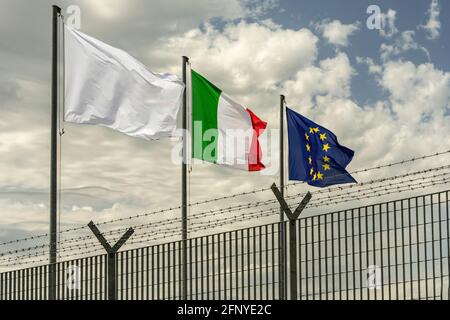 Drei Flaggen, die von Europa, die von Italien und eine weiße, hinter einem Zaun mit Stacheldraht. Fucino, Abruzzen, Italien, Europa Stockfoto