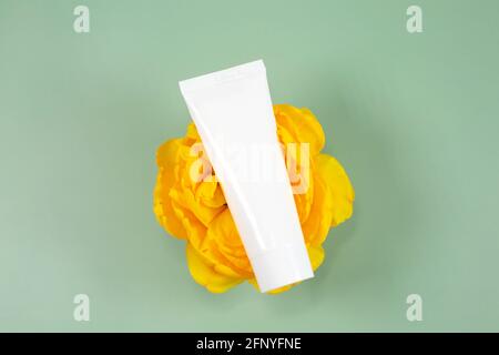 Weiße Kosmetikröhre auf einer schönen gelben Blume auf grünem Hintergrund. Produktkonzept für natürliche Schönheit. Banner-Mockup für Beauty-Blog. Flach liegend, Draufsicht. Stockfoto