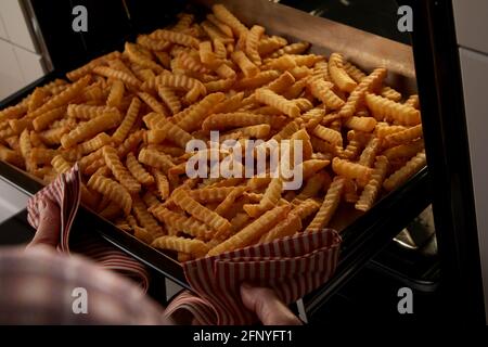 Von oben Erntegut Person mit Handtuch nehmen Tablett mit knusprig Zerkrinken Sie Pommes aus dem heißen Ofen, während Sie das Mittagessen zu Hause zubereiten Stockfoto