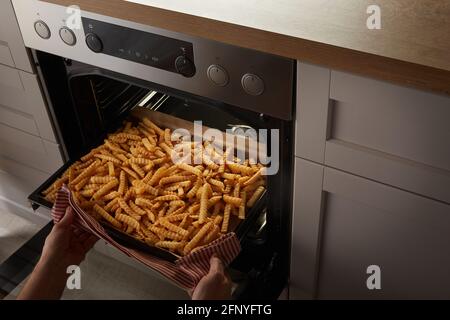 Von oben anonymen Person mit Handtuch nehmen Tablett mit knusprig Zerkrinkle Pommes vom heißen Herd Stockfoto