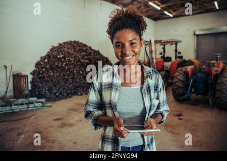 Gemischte Rasse weibliche Eingabe auf digitalen Tablet stehen in der Farm Scheune mit kariertem Flanell Stockfoto