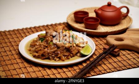 Nahaufnahme von Stir frittierten Noodle mit süßem Soja Sauce (Pad siehe EW) auf Bambus-Tischset mit Teeset Stockfoto