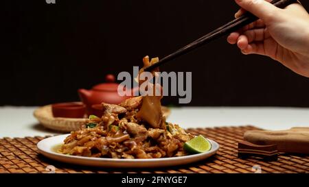 Nahaufnahme der weiblichen Hand, die den Essstäbchen zum Essen hält Gebratener Noodle mit süßer Sojasauce umrühren (Pad siehe EW) Stockfoto