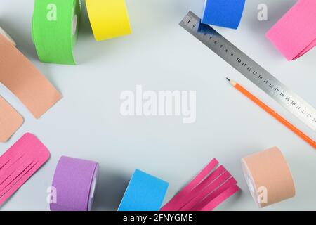 Buntes Kinesiologieband, Schere, Bleistift, Lineal und verschiedene Formschnitte für Applikationen auf blauem Hintergrund. Kinesiologie taping Lymphausfluss und Spee Stockfoto