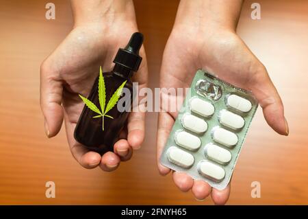 Therapeutisches Marihuana-Konzept: Hände, die natürliches CBD-Öl aus Cannabis und traditionellen Medikamenten zeigen und vergleichen. Stockfoto