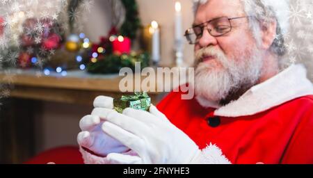 Komposition von Sternen über dem weihnachtsmann, der ein kleines weihnachtsgeschenk hält Stockfoto