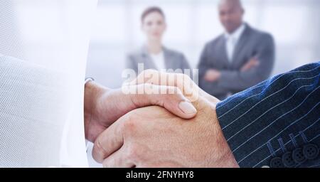 Mittelteil von zwei Geschäftsleuten, die sich vor technischem Hintergrund die Hände schütteln Stockfoto