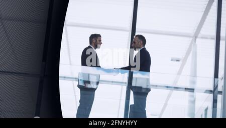 Technologie-Hintergrund über zwei Geschäftsleute, die sich im modernen Büro die Hände schütteln Stockfoto