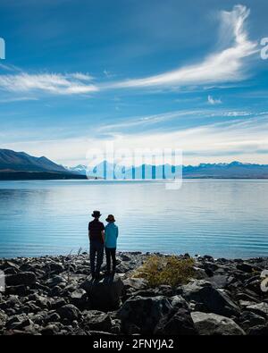 Pärchen, die am Ufer des Lake Pukaki stehen und die Aussicht auf Mt Cook und die südlichen Alpen, Südinsel, genießen. Vertikales Format. Stockfoto