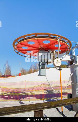 Großes Metallrad mit Motor für die Bewegung des Seilzugkabels. Antriebsmechanismus gegen den blauen Himmel. Berghang Ausrüstung für Snowboarden. Skitouren an einem sonnigen Tag. Stockfoto