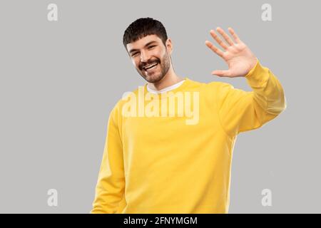 Lächelnder junger Mann in gelbem Sweatshirt mit winkender Hand Stockfoto