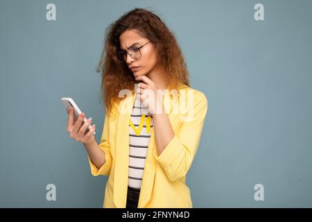 Schöne junge Frau trägt Freizeitkleidung isoliert über Hintergrund stehen Surfen im Internet über das Telefon mit Blick auf mobile Bildschirm Stockfoto