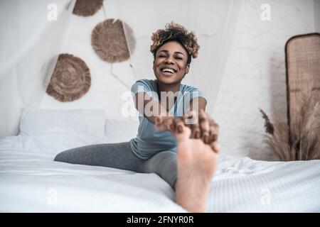 Lachende Frau, die auf dem Bett sitzt und sich bis zum Bein beugt Stockfoto