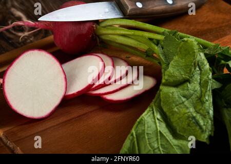 Frisch geschnittener roter Rettich auf einem Holzbrett mit dem Messer an der Seite. Stockfoto