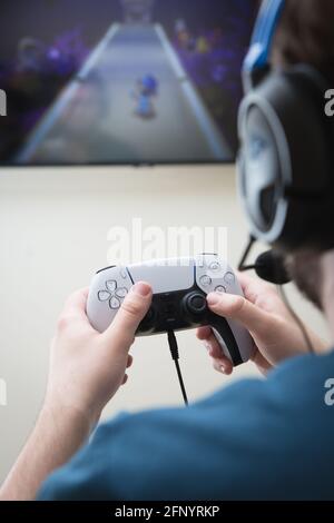 YORK, GROSSBRITANNIEN - 9. MAI 2021. Rückansicht eines Teenagers mit einem PlayStation 5-Gamecontroller und Online-Videospielen mit Kopfhörern und Mikrofon Stockfoto