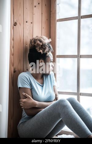 Einsame traurige Frau, die aus dem Fenster auf der Fensterbank schaut Stockfoto