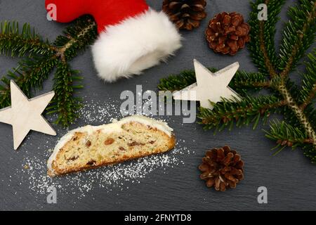 weihnachtsstollen mit Tannenzweig, weihnachtsmannschuh und Sternen, die zur weihnachtszeit auf schwarzem Schiefer liegen Stockfoto