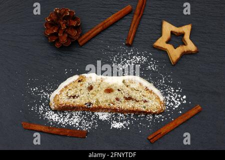weihnachtsstollen mit Tannenzapfen, Sternen und Zimtstangen, die zur weihnachtszeit auf schwarzem Schiefer liegen Stockfoto