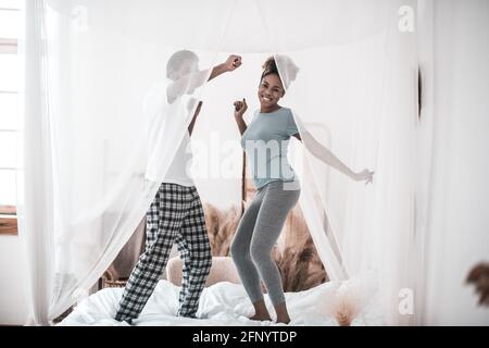 Fröhlicher Mann und Frau im Schlafanzug, die auf dem Bett tanzen Stockfoto
