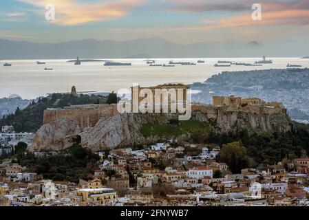 Die Akropolis von Athen mit Parthenon-Tempel vom Lycabettus-Hügel aus gesehen. Plaka-Viertel unter der Akropolis. Schiffe vertäuten vor dem Hafen von Piräus. Sonnenuntergang Stockfoto