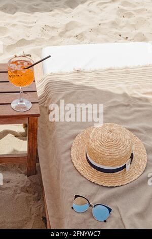 Ein Glas aperol Spritz, Strohhut und Sonnenbrille am Strand Stockfoto