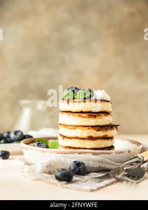 Gebratene Hüttenkäse-Pfannkuchen oder Krapfen mit frischer Heidelbeere und saurer Rahm auf einem Teller. Glutenfrei. Traditionelles Frühstück mit ukrainischen und russischen Speisen Stockfoto