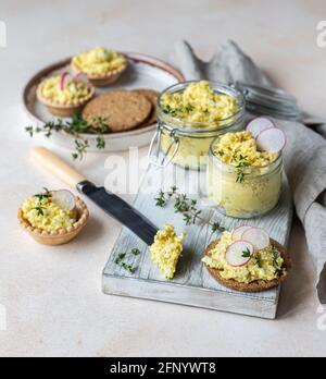 Tartlets mit Eierpastete oder Salat und Rettich und Thymian auf hellem Steingrund. Eiertopf im Glasgefäß. Selektiver Fokus. Stockfoto