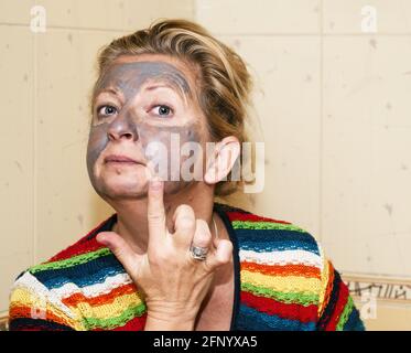 Reife Frau Anwendung schwarzen Ton Gesicht Peeling Maske in der Badezimmer Stockfoto