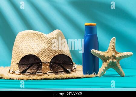 Damen Strohhut, Sonnenbrille, Sonnencreme und Seesterne auf farbigem Hintergrund. Stockfoto