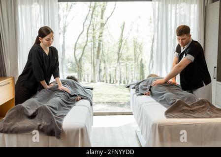 Zwei Masseure, die eine tiefe Rückenmassage für die Gäste mit Verwöhntechnik machen. Wellness und Freizeit für die Gesundheit zusammen mit Waldblick im Fenster. Stockfoto