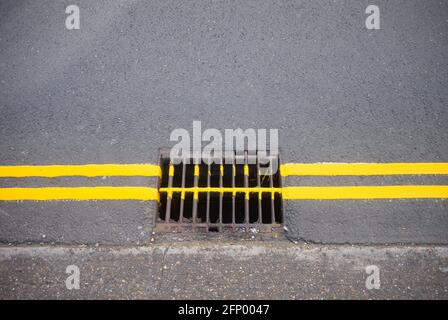 Doppelte gelbe Linien gehen über einen Abfluss in der Straße Stockfoto
