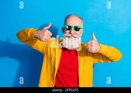 Foto von fröhlich lächelnd gute Laune Großvater in der Sonnenuhr zeigt Daumenaufdruck isoliert auf blauem Hintergrund Stockfoto